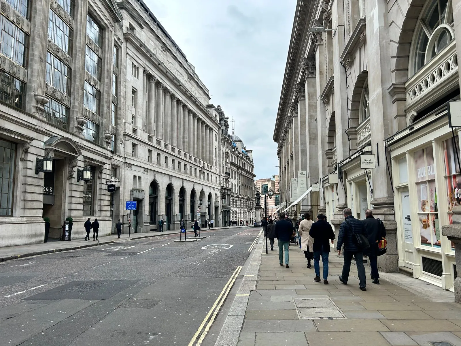 People walking along a city street with historic architecture in an urban setting.